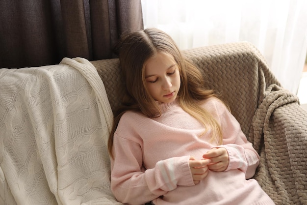 a teenage girl in jeans and a pink sweater is sitting very sad on the couch Highquality photograp