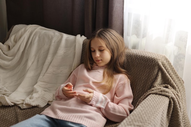 a teenage girl in jeans and a pink sweater is sitting very sad on the couch Highquality photograp