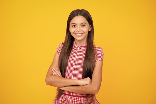 Teenage girl kid with crossed arms looking at camera isolated on yellow studio background