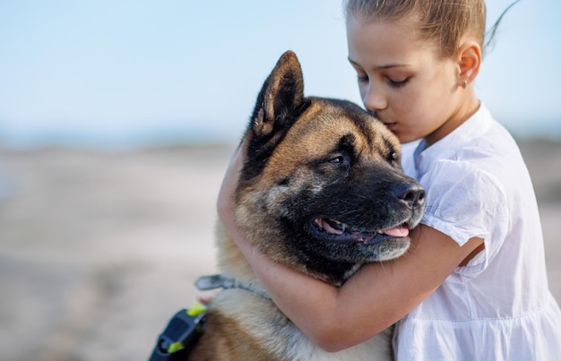 Teenage girl in light clothes hugs and loves dog friend of Akita Inu breed on beach near Black Sea in warm sunny weather