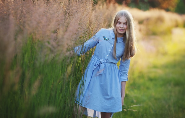 Teenage girl long hair on the grass Pretty happy girl enjoying summer and sunny weather in park beautiful model in casual short blue dress on the field in sun light the child has braces