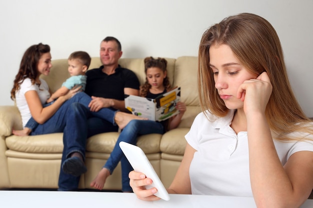 Teenage girl looks in the phone alone on the background of communicating family