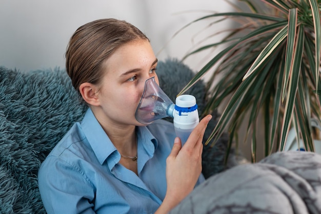 Teenage girl makes inhalation with a nebulizer equipment. Sick child holding inhalator in hand and breathes through an inhaler at home