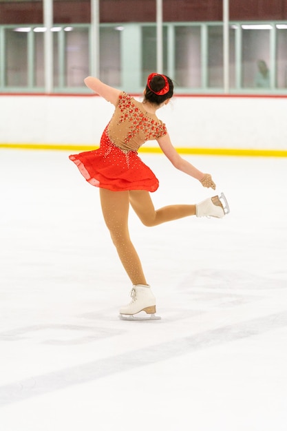 Teenage girl practicing figure skating on an indoor ice skating rink.