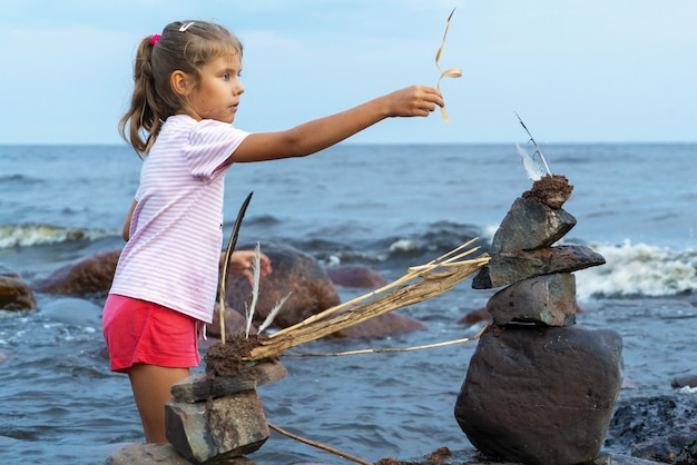 A teenage girl puts twigs and feathers on the stones in pyramids on the lake shore