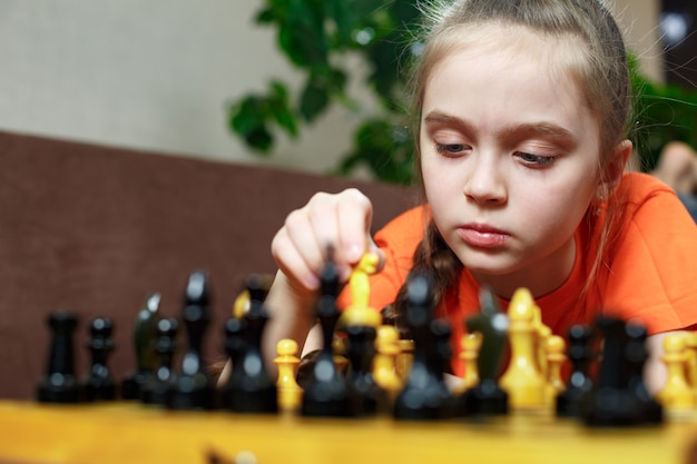 A teenage girl during quarantine plays chess at home lying on the sofa.