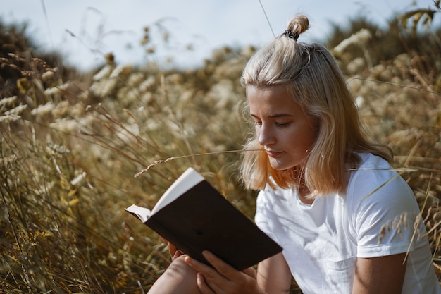 Teenage girl reading the book in the field. The girl sitting on a grass, reading a book. Rest and reading