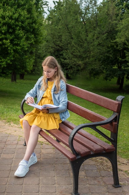 Teenage girl reads a book on a bench in the summer park Vertical photo