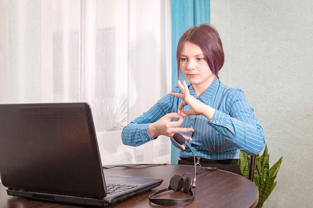 A teenage girl sits in front of her laptop learning sign language, a language for the deaf and dumb online.