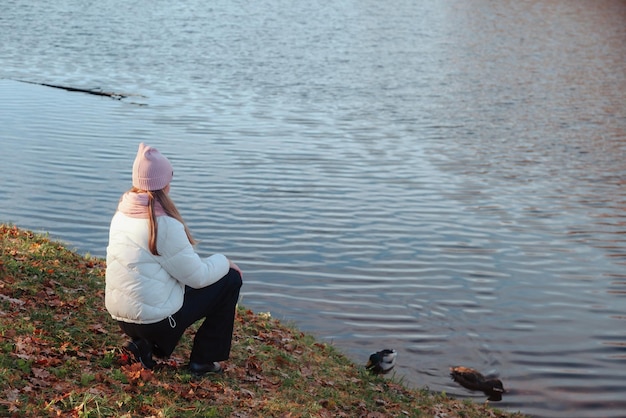 Teenage girl sitting from behind wearing casual fall clothes in an autumn park with lake outdoors