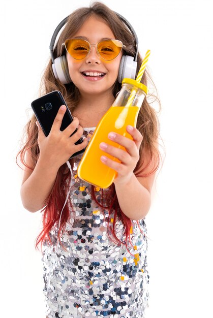 Teenage girl in sparkling dress and yellow sunglasses, with big white earphones