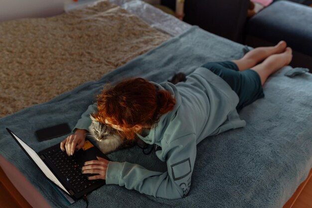 Teenage girl spending time together with cat lying on bed using laptop