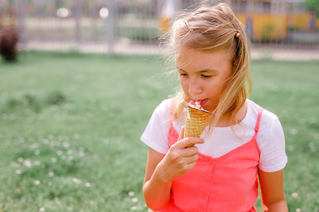 Teenage girl in summer dress sitting on the grass eating ice cream