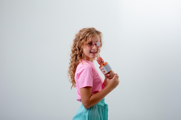 A teenage girl in sunglasses holds a microphone and sings a song on a white background