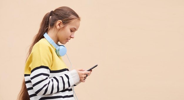 Teenage girl in a sweater uses a mobile phone against a colored wall