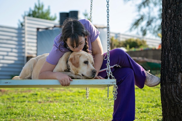 A teenage girl swings on a swing with her old Labrador dog