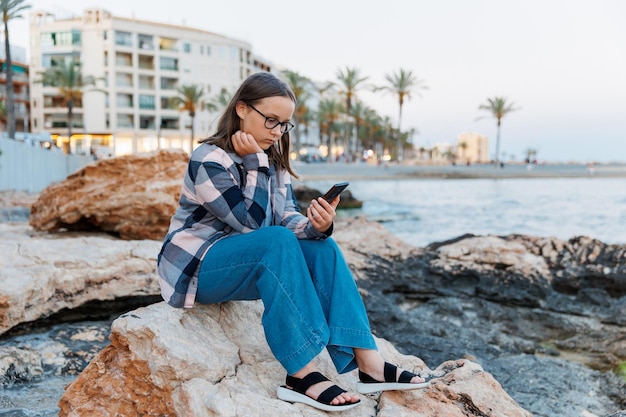 A teenage girl talks on the phone against the backdrop of city and the sea on a hot evening