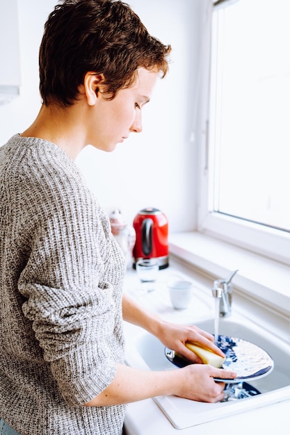 Teenage girl washing dishes in kitchen sink