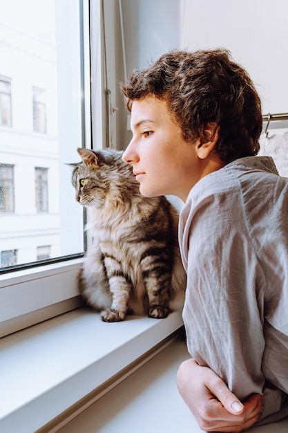 Teenage girl with beloved cat look out window together