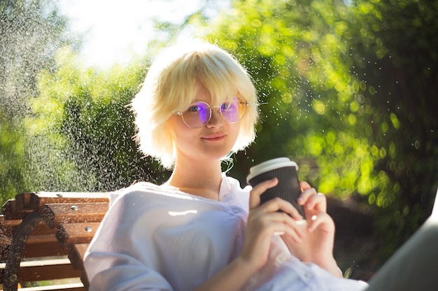 Teenage girl with blond hear drinking coffee from craft paper cup outside