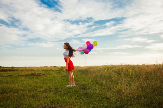 Teenage girl with colourful balloons stands at the meadow, place for text or inspirational quote