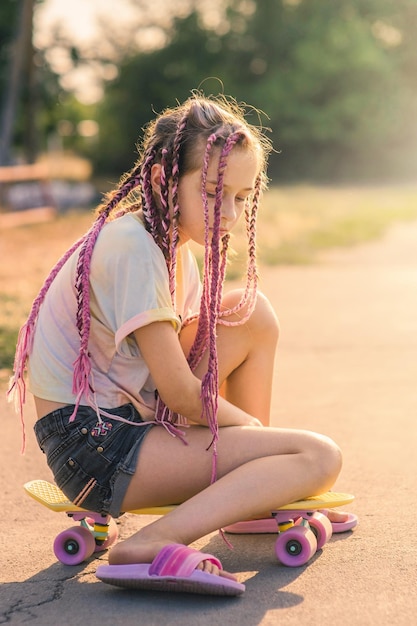 A teenage girl with pink pigtails sat down on a penny board and thought A girl on a sunny day