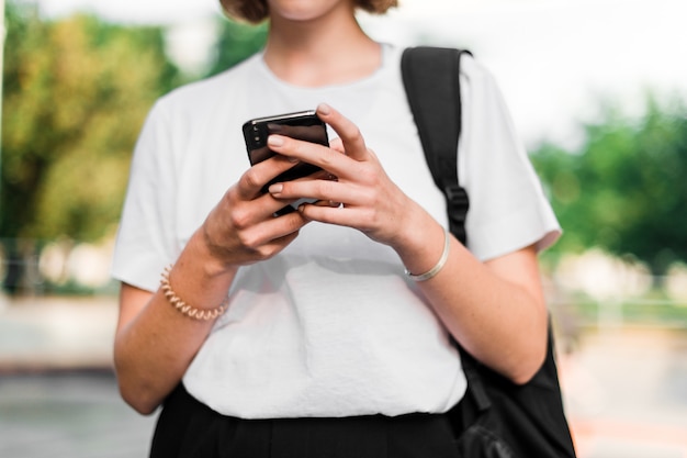 Teenage girl with school backpack and phone on the campus after studies using phone