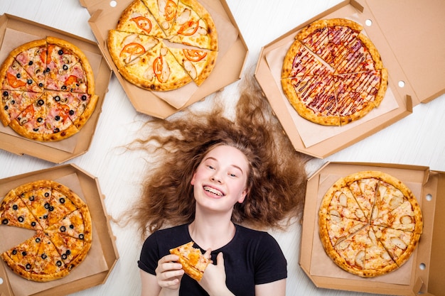 teenage girl with a slice of pizza in her hands and pizza boxes around her lies