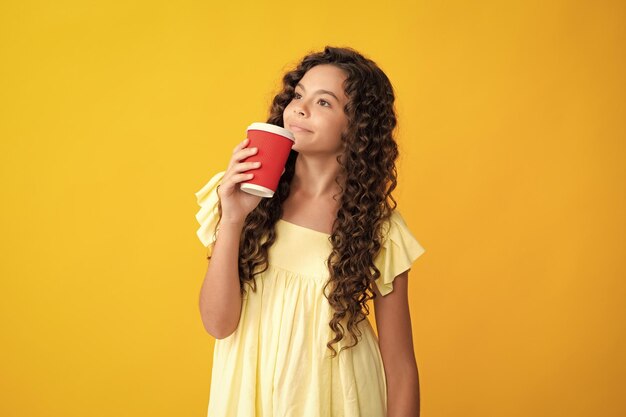 Teenage girl with take away cup of cappuccino coffee or tea Child with takeaway cup on yellow background morning drink beverage Happy teenager portrait Smiling girl