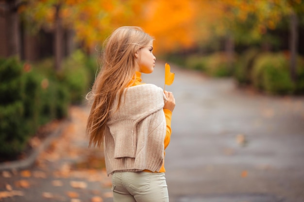 a teenage girl in a yellow sweater walks along a street outside the city against the backdrop of yellow trees fun walk in autumn