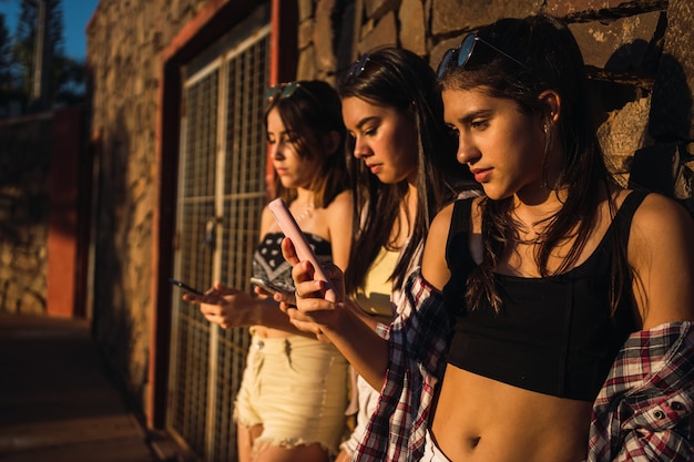 Teenage girls leaning against a wall looking at their mobile phones and texting with their smartphones