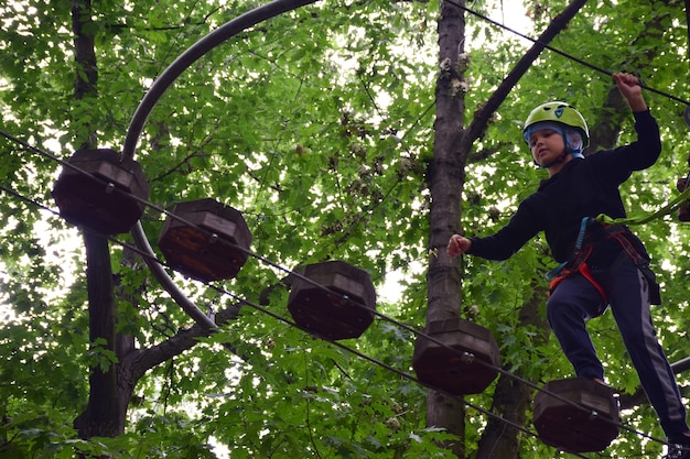 A teenage guy climbs a hanging ladder in a rope amusement park