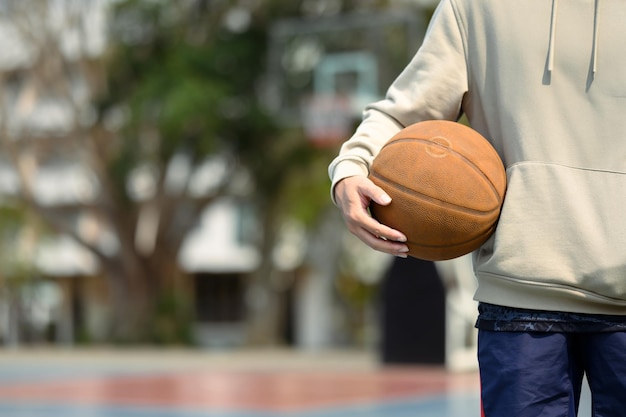 Teenage man holding a ball standing on the basketball court Sport and active lifestyle concept