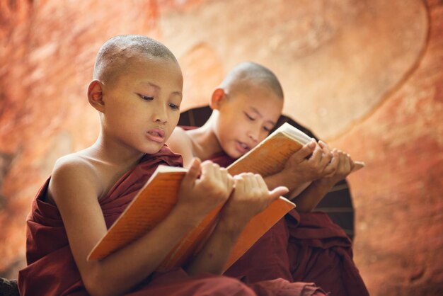 Photo teenage monks reading books against wall