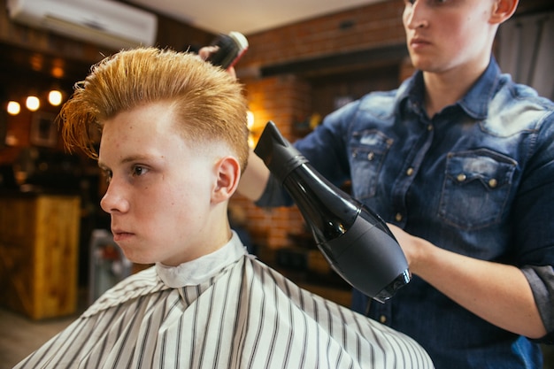 Teenage redhead boy haircuts hairdresser in the Barber shop. Fashionable stylish retro hairstyle. Portrait of a child with a beautiful haircut. Russia, Sverdlovsk, February 12, 2019