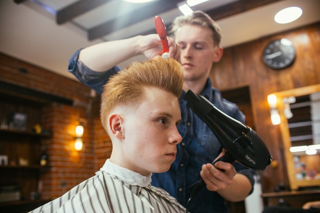 Teenage redhead boy haircuts hairdresser in the Barber shop. Fashionable stylish retro hairstyle. Portrait of a child with a beautiful haircut. ,  , 