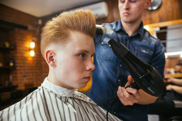 Teenage redhead boy haircuts hairdresser in the Barber shop. Fashionable stylish retro hairstyle. Portrait of a child with a beautiful haircut.