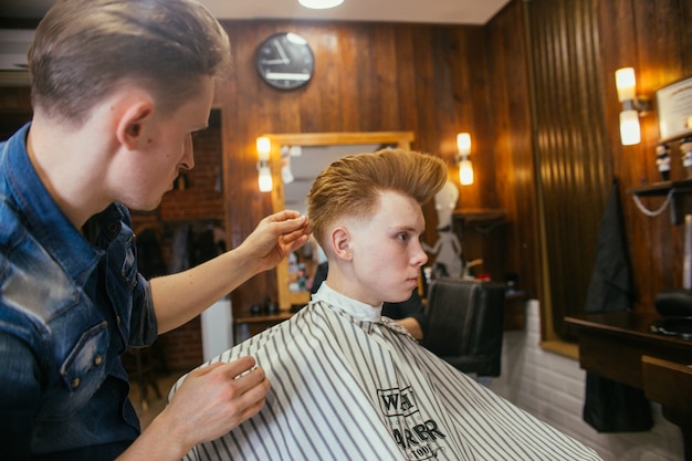 Teenage redhead boy haircuts hairdresser in the Barber shop.