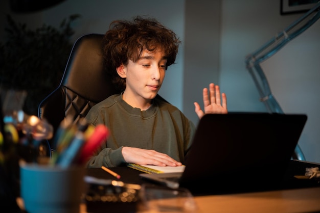 Teenage remote college distance learning boy waves hand to online tutor on laptop screen