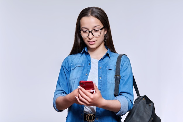 Teenage student with backpack smartphone looking at screen on light ackground