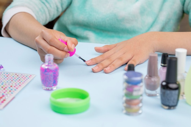 Teenage woman painting her nails at home with nail supplies on the table