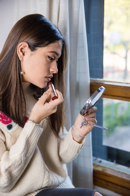 A teenager applying a lipstick with a mirror in her hand