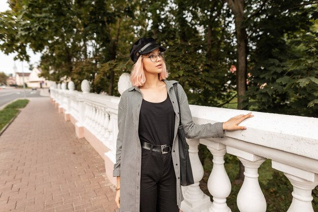 Teenager beautiful young woman in fashion casual clothes with glasses and a cap is walking on the street