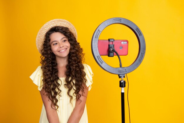 Teenager blogger making video child vlogger influencer record content Child blogger records video on mobile phone using ring video lamp Happy teenager positive and smiling emotions of teen girl