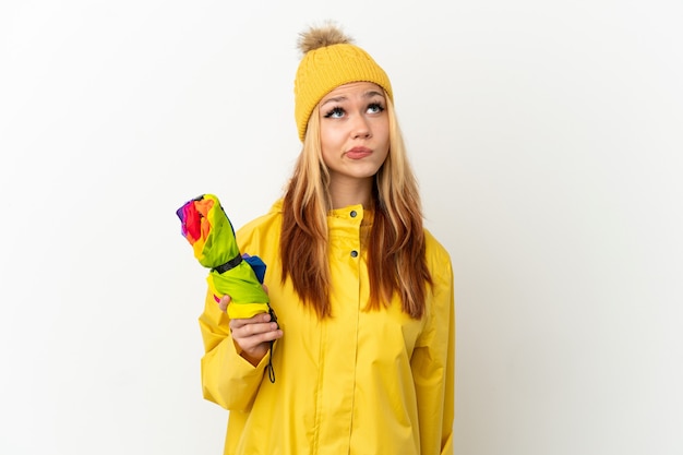 Teenager blonde girl wearing a rainproof coat over isolated white background and looking up