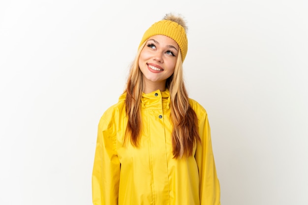 Teenager blonde girl wearing a rainproof coat over isolated white background thinking an idea while looking up