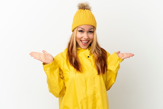 Teenager blonde girl wearing a rainproof coat over isolated white background with shocked facial expression