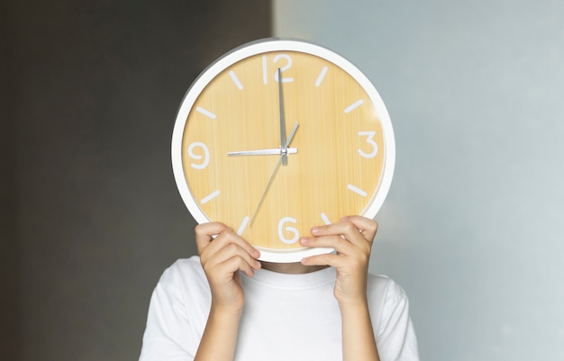 A teenager boy holds a big clock in his hands.