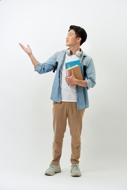 Teenager boy is listening for music holding books and standing on white background