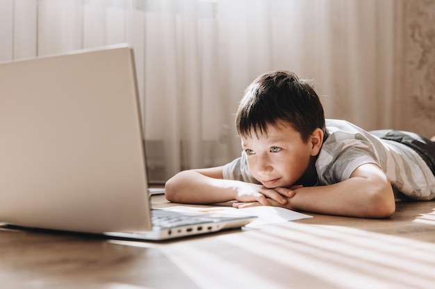 Teenager boy in lying on floor with laptop having video call and online lesson at home Schoolboy studying homework Distance education remote training concept